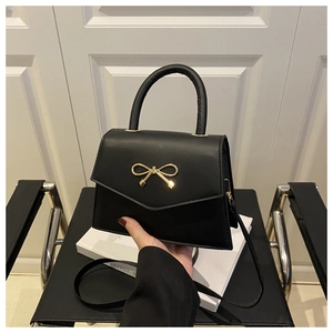 Detailed view of black leather mini square bag with golden bow clasp and round handle
