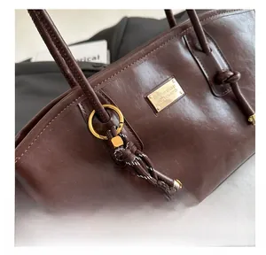 Macro view of dark brown leather tote bag detail with gold plate and woven pendant charm
