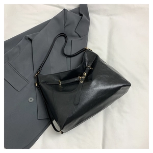 Detail of black leather shoulder bag with gold hardware on a grey suit background