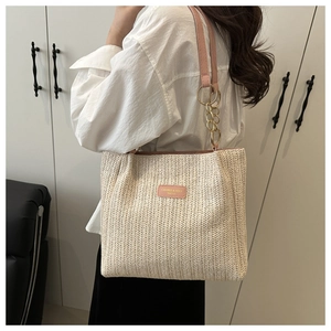 Detail of woven straw tote bag featuring pink leather strap and golden metal chain handle