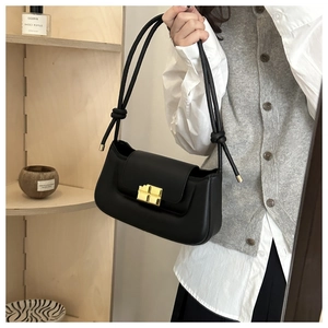 Close-up of matte black rectangular handbag featuring a vintage gold buckle and knotted strap