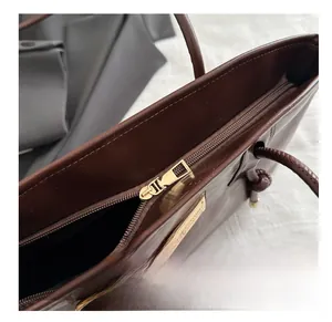 Close-up of golden metal zipper and logo plate on a dark brown vintage tote bag