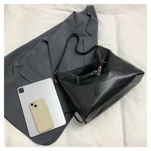 Detailed view of large black leather tote bag with tablet and phone on grey blazer