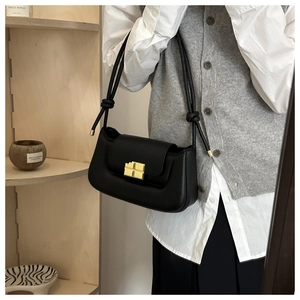 Detail of minimalist black underarm bag featuring a knotted strap and gold square lock