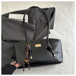 Detail of black PU leather tote bag with golden logo plate and woven rope charm