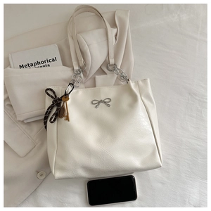 Detail of cream tote bag with silver bow, chain strap and aesthetic tennis racket charm