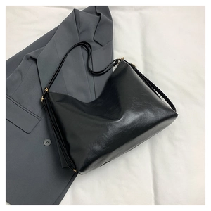 Detail of a black glossy hobo bag on a grey suit with adjustable gold buckle