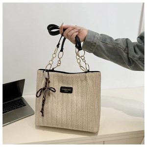 Detail of woven straw tote bag featuring gold chain handle and tennis racket charm