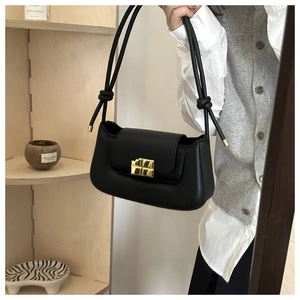 Detail of black leather baguette bag with gold cross buckle and knot shoulder strap design