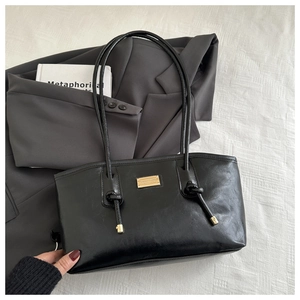 Close-up of black glossy leather tote bag featuring a golden metal logo plate and knot detail