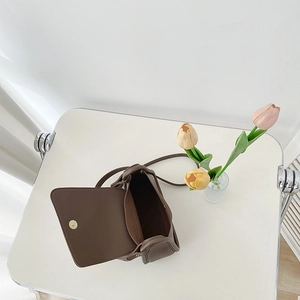 Brown PU leather square crossbody bag with gold magnetic buckle on a white desk