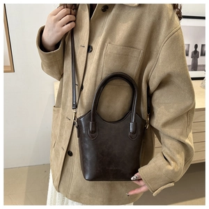 Detailed close-up of dark brown leather bucket bag with embossed logo on beige coat