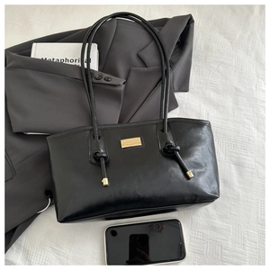 Detail of a black shiny leather tote bag featuring a gold logo plate and knotted strap