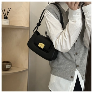 Detail of black leather underarm bag with gold metal lock and knotted strap design