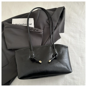 Detail of black underarm tote bag showing knot handle and gold hardware on blazer