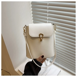 Detail of white bucket bag with gold clasp held against a minimalist background