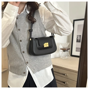Detail of a black leather square bag with a gold cross lock and knotted strap design