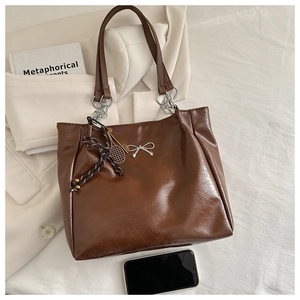 Detail of a brown leather tote bag featuring chain straps and decorative pendants