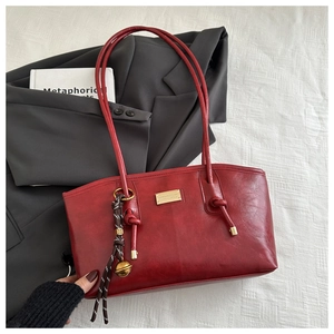 Detail of vintage burgundy shoulder bag featuring a gold plaque and braided tassel