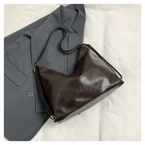 Detail of dark brown oil wax leather tote bag with gold hardware on a grey blazer