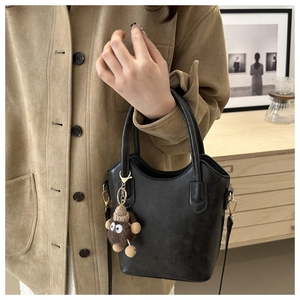 Detail of black faux leather bucket bag with plush charm and long strap carried by a model