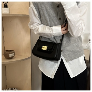 Detail shot of a black leather shoulder bag with gold buckle worn by a model in a minimal setting