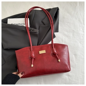 Detail of burgundy tote bag with gold metal plate and knotted strap on blazer background