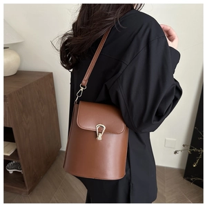 Détail d'un sac seau en cuir marron avec boucle dorée porté par un mannequin de côté
