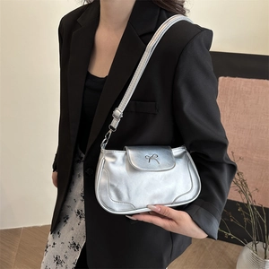 Retro silver metallic shoulder bag with bow detail worn by a model in a modern room
