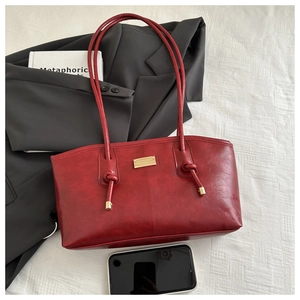 Detail of dark red faux leather tote bag with gold metal plate and knotted shoulder strap