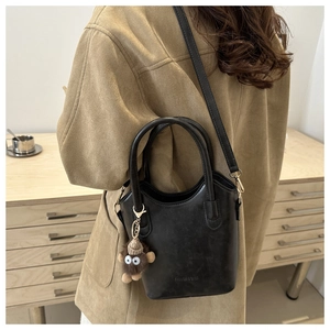Detail of black leather bucket bag with plush monkey charm worn with camel wool coat