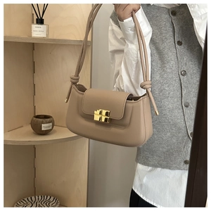 Detail of minimalist beige baguette bag with architectural gold clasp and knotted strap