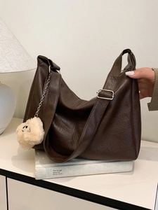 Large dark brown leather tote bag with plush charm on minimalist studio background