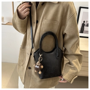 Detail of black vintage bucket bag with plush monster charm on khaki coat