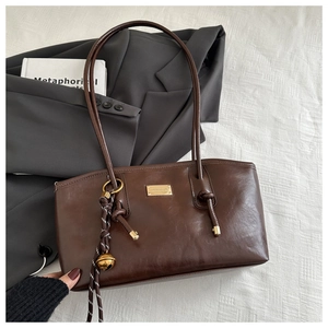 Detail of dark brown vintage oil-wax tote bag with gold metal logo and bell charm