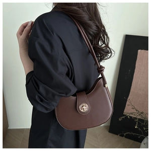 Détail d'un sac demi-lune en cuir marron avec fermoir rotatif doré et bandoulière nouée