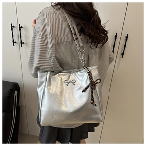 Detail of silver metallic tote bag featuring bow hardware and chain leather strap on a model