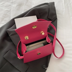 Mini-Umhängetasche in Magenta mit Schleife auf grauem Anzug, zeigt Platz für Handy
