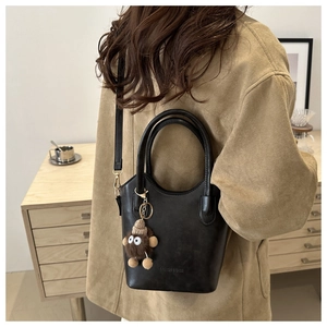 Detail of black leather bucket bag featuring a plush monster charm and embossed fashion text