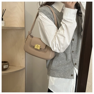 Detail view of chic beige leather saddle bag with gold metal clasp on model