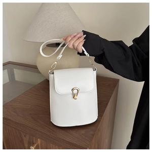 Close-up of white leather bucket bag featuring a gold metal buckle and flap design