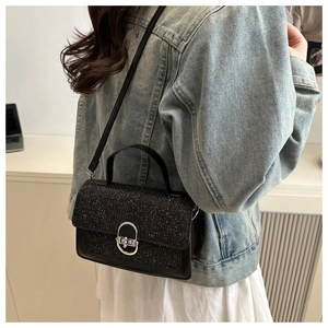 Detail of black shimmer crossbody bag with silver oval metal twist lock and sequin texture