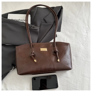 Detail view of deep brown vintage shoulder bag with golden brand plaque and slim strap