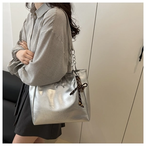 Detail of silver metallic tote bag with metal bow and textured charm for commuting