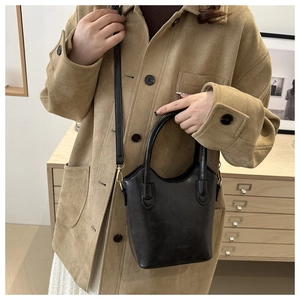 Detail of a black leather bucket bag with gold hardware worn over a khaki jacket
