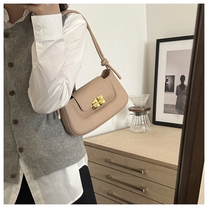 Detail of a chic cream leather baguette bag featuring a gold twist lock and knotted strap