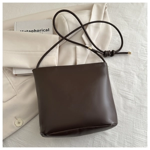 Detail of dark chocolate leather crossbody bag with slim cord strap on cream blazer