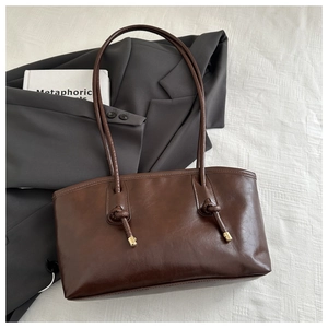 Detail of dark brown leather tote bag with knotted strap and gold metal tip