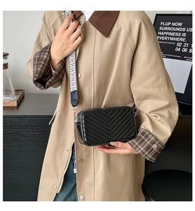Sac bandoulière noir matelassé avec sangle géométrique porté sur un trench-coat kaki