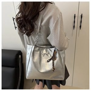 Detail of silver tote bag with metallic bow and woven key charm on textured faux leather